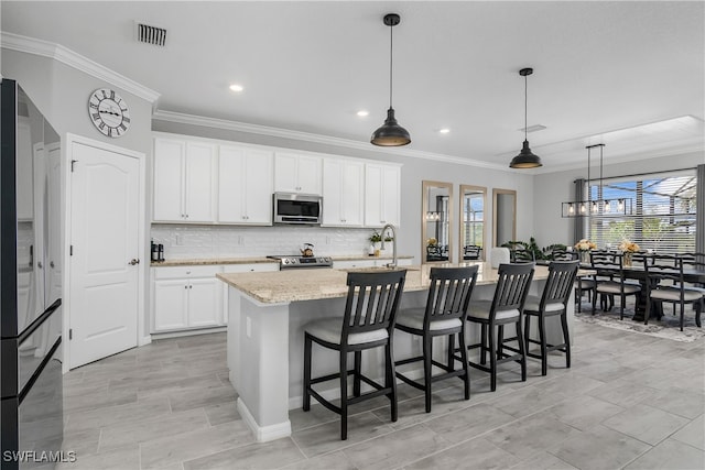 kitchen featuring a kitchen island with sink, white cabinets, decorative light fixtures, light stone counters, and stainless steel appliances