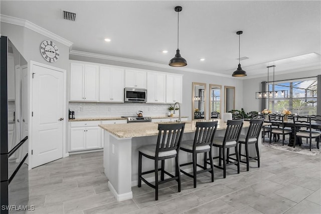 kitchen with visible vents, a kitchen island with sink, ornamental molding, backsplash, and appliances with stainless steel finishes