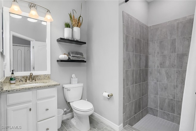 bathroom featuring tiled shower, toilet, vanity, and baseboards