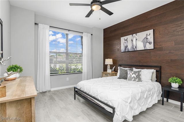 bedroom featuring wood walls, an accent wall, baseboards, and ceiling fan