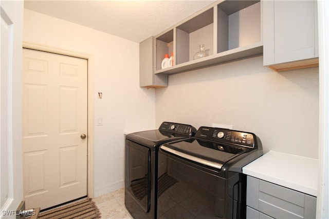 laundry area featuring washer and clothes dryer, a textured ceiling, light tile patterned floors, and cabinets