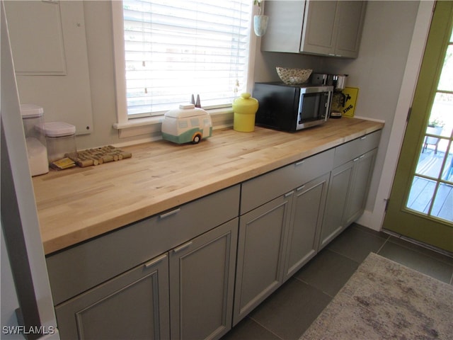 kitchen featuring butcher block countertops, dark tile patterned flooring, and gray cabinetry