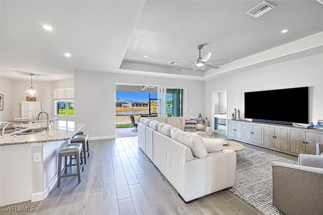 living room with sink, a raised ceiling, and ceiling fan