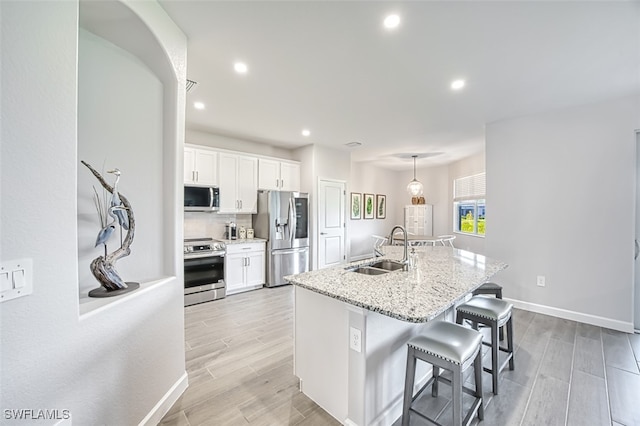 kitchen featuring stainless steel appliances, white cabinetry, sink, and an island with sink