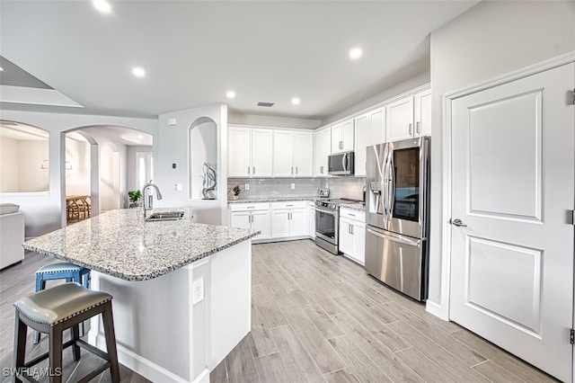 kitchen with a kitchen breakfast bar, a center island with sink, stainless steel appliances, light stone countertops, and white cabinets