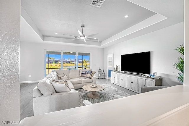 living room with ceiling fan, hardwood / wood-style floors, and a tray ceiling