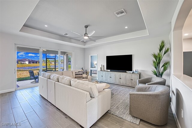 living room featuring a raised ceiling and ceiling fan