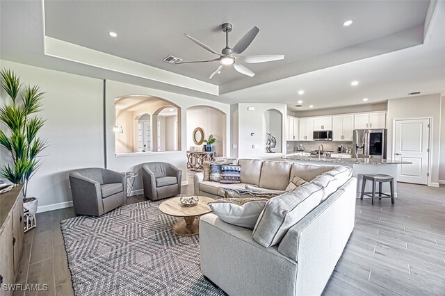 living room with ceiling fan and a tray ceiling