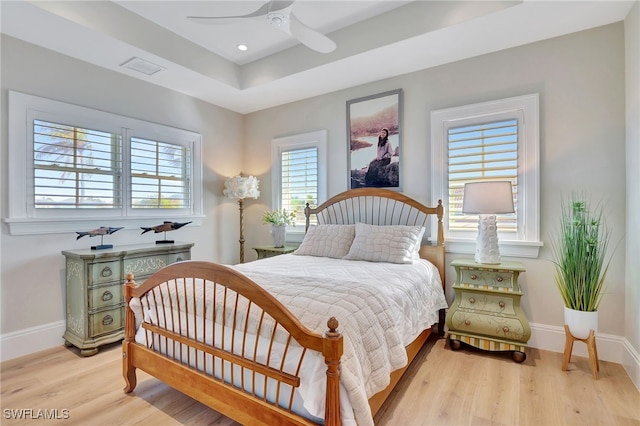 bedroom with light wood finished floors, baseboards, a tray ceiling, recessed lighting, and a ceiling fan