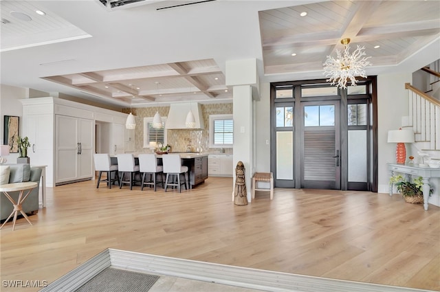 entrance foyer featuring beam ceiling, an inviting chandelier, coffered ceiling, and light hardwood / wood-style flooring