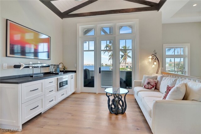 living room featuring lofted ceiling with beams, a water view, and light wood-type flooring