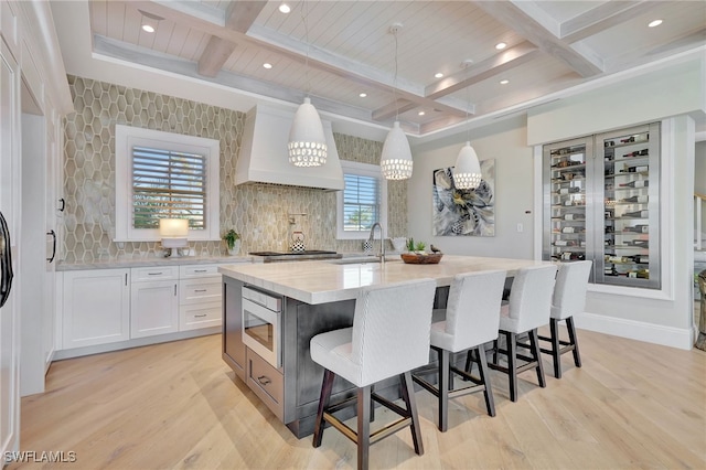 kitchen featuring stainless steel appliances, premium range hood, light wood-style flooring, white cabinets, and beam ceiling