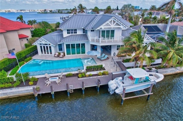 rear view of property with a balcony, a standing seam roof, a water view, and a pool with connected hot tub