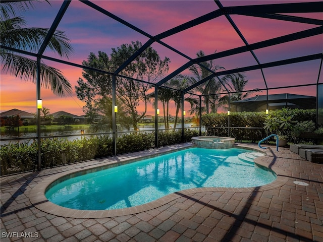 pool at dusk featuring an in ground hot tub, a patio area, a water view, and glass enclosure