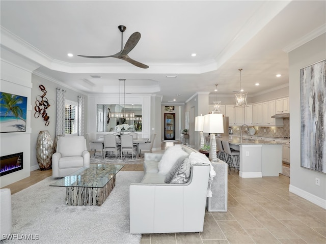 tiled living room featuring ornamental molding, a tray ceiling, and ceiling fan with notable chandelier