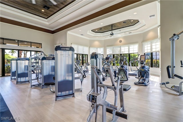 gym with a towering ceiling, light hardwood / wood-style floors, a tray ceiling, and ceiling fan