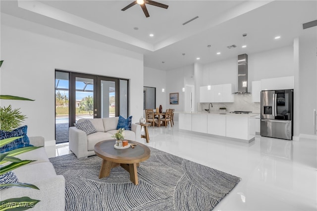 tiled living room featuring a towering ceiling, sink, french doors, a tray ceiling, and ceiling fan