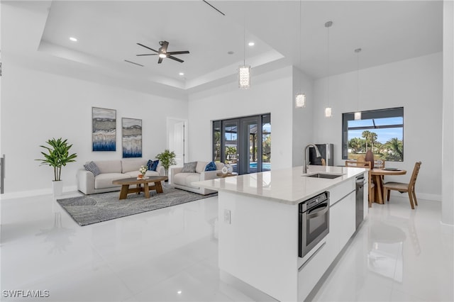 kitchen featuring an island with sink, hanging light fixtures, sink, a raised ceiling, and white cabinetry