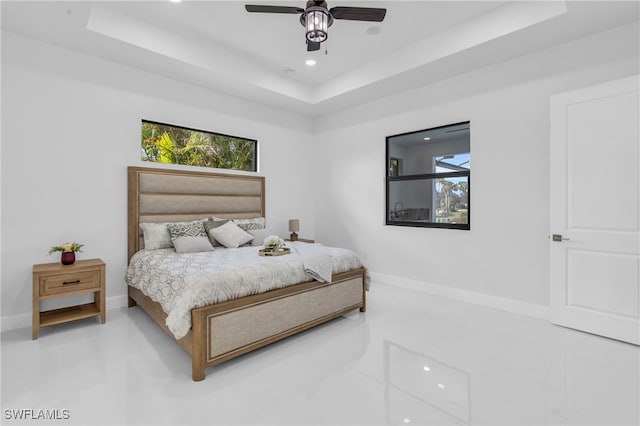 bedroom with multiple windows, a tray ceiling, and ceiling fan