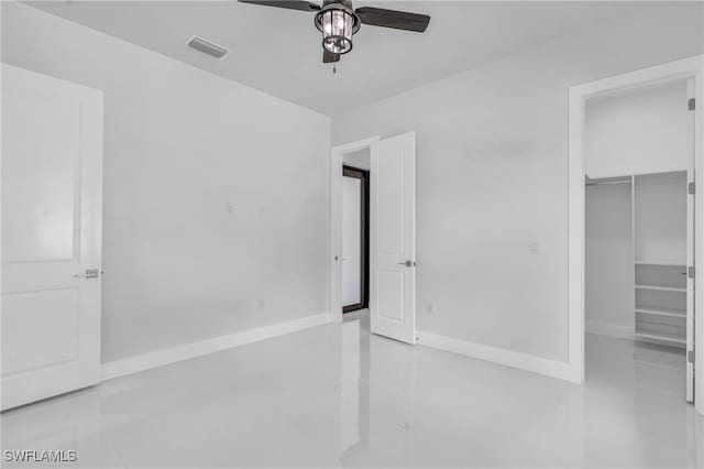 unfurnished bedroom featuring a spacious closet, light tile patterned flooring, a closet, and ceiling fan