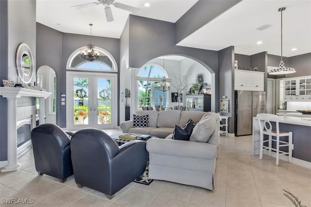 tiled living room with a high ceiling, ceiling fan with notable chandelier, and french doors