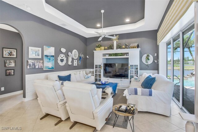 living room with light tile patterned floors, ceiling fan, and a tray ceiling