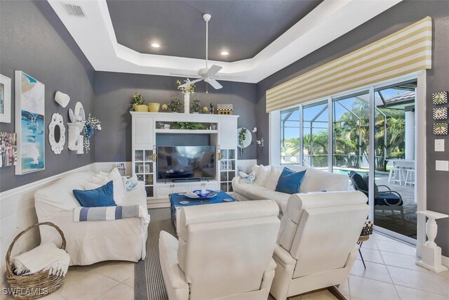 living room with light tile patterned flooring, ceiling fan, and a tray ceiling