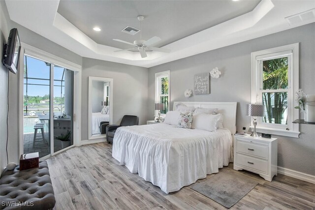 bedroom with a tray ceiling, light hardwood / wood-style floors, and multiple windows