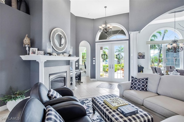 tiled living room featuring a tiled fireplace, french doors, a chandelier, and a high ceiling