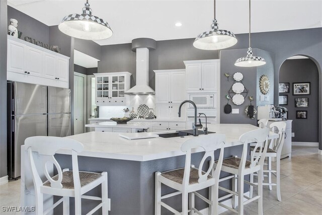 kitchen with a spacious island, wall chimney exhaust hood, hanging light fixtures, stainless steel fridge, and white microwave