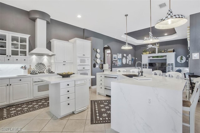 kitchen featuring white cabinetry, white appliances, a tray ceiling, and an island with sink