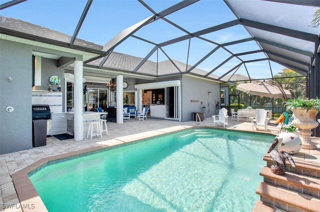 view of swimming pool with exterior kitchen, an outdoor bar, glass enclosure, and a patio area