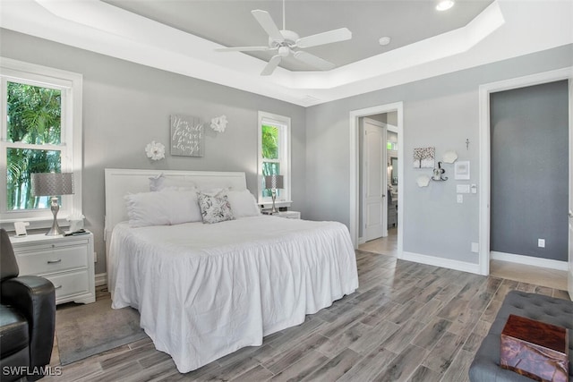 bedroom with a raised ceiling, multiple windows, ceiling fan, and light hardwood / wood-style flooring