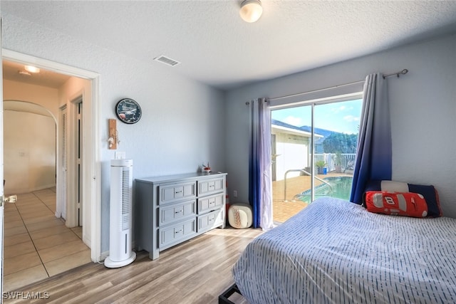 bedroom with access to exterior, light hardwood / wood-style flooring, and a textured ceiling