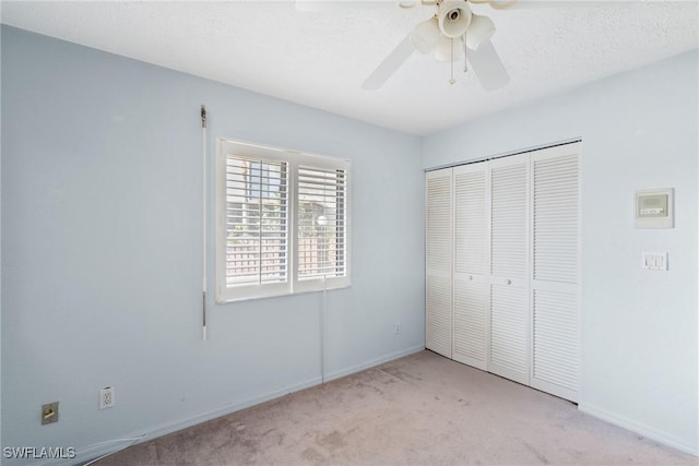 unfurnished bedroom featuring light carpet, a textured ceiling, a closet, and ceiling fan