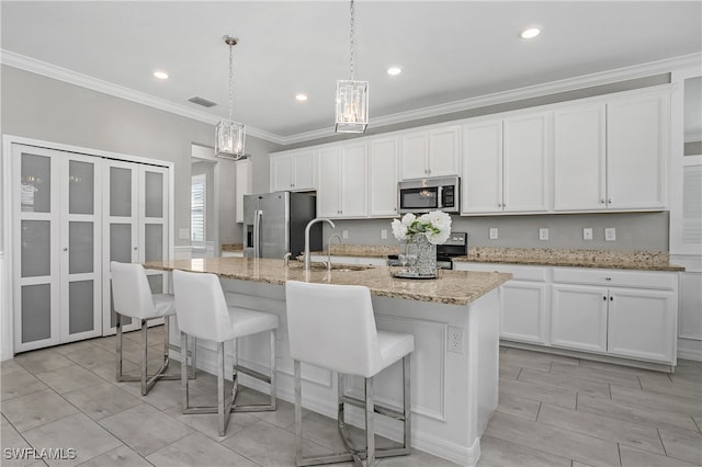 kitchen featuring white cabinets, hanging light fixtures, an island with sink, and stainless steel appliances