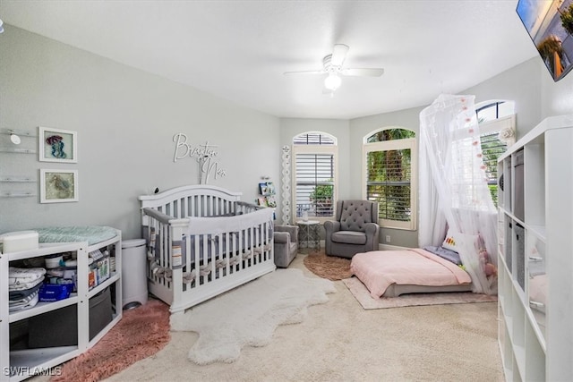 carpeted bedroom with a crib and ceiling fan