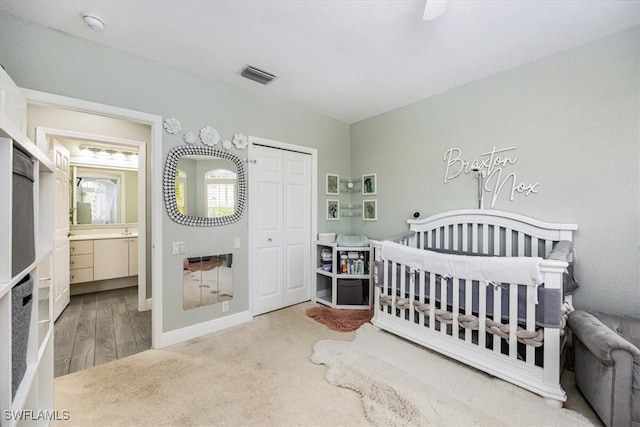 bedroom featuring ensuite bathroom, ceiling fan, wood-type flooring, a nursery area, and a closet