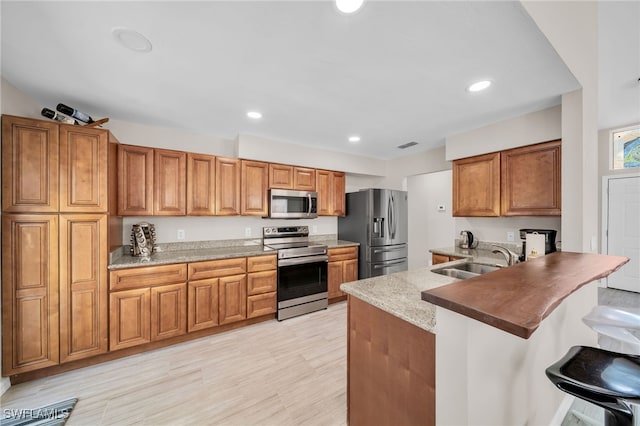 kitchen featuring a kitchen breakfast bar, kitchen peninsula, stainless steel appliances, sink, and light hardwood / wood-style floors