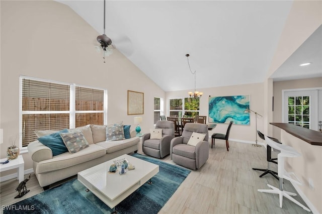 living area featuring ceiling fan with notable chandelier, high vaulted ceiling, a healthy amount of sunlight, and baseboards