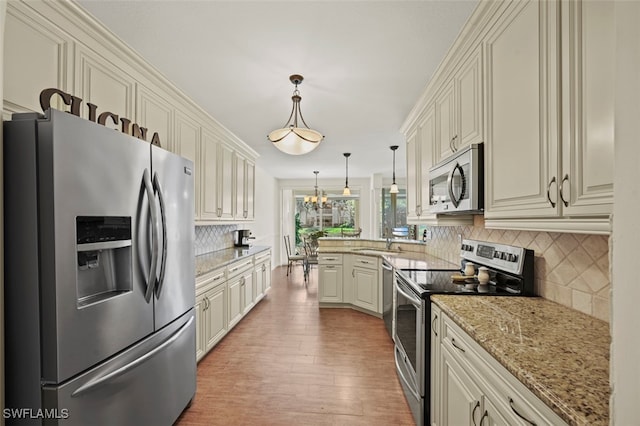 kitchen with appliances with stainless steel finishes, light hardwood / wood-style flooring, a notable chandelier, light stone counters, and decorative light fixtures