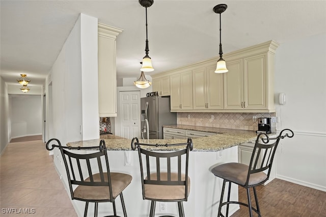 kitchen featuring light stone counters, cream cabinetry, stainless steel fridge with ice dispenser, kitchen peninsula, and decorative backsplash