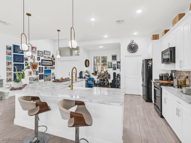 kitchen featuring light hardwood / wood-style floors, decorative light fixtures, white cabinets, and black appliances