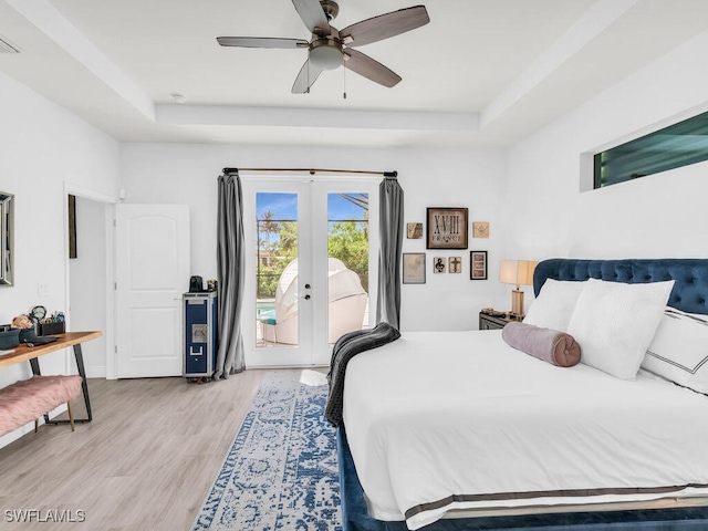 bedroom featuring light hardwood / wood-style flooring, access to outside, a raised ceiling, and ceiling fan