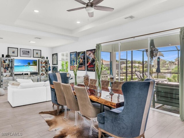 dining area with ceiling fan, a tray ceiling, and light wood-type flooring