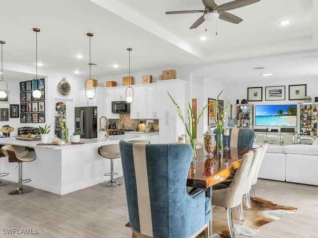 dining space featuring ceiling fan, sink, and light wood-type flooring