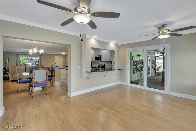 living area with light wood finished floors, baseboards, crown molding, and ceiling fan with notable chandelier