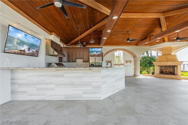 exterior space featuring backsplash, wall chimney exhaust hood, exterior fireplace, wooden ceiling, and light stone counters