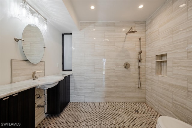 bathroom with tile walls, vanity, a tile shower, and toilet