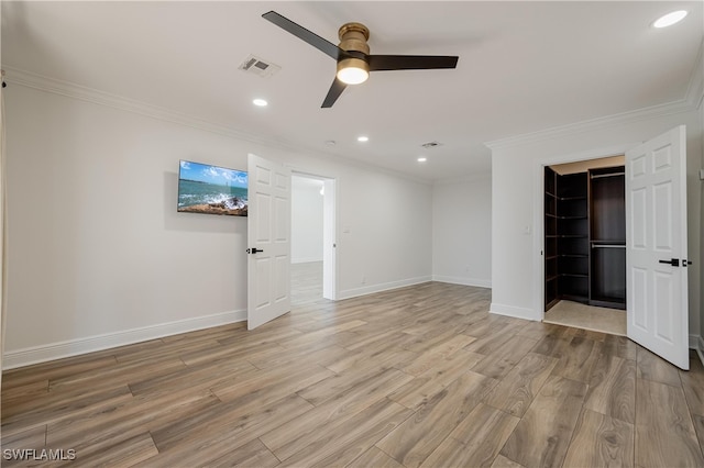 unfurnished bedroom featuring a closet, a spacious closet, crown molding, light hardwood / wood-style floors, and ceiling fan